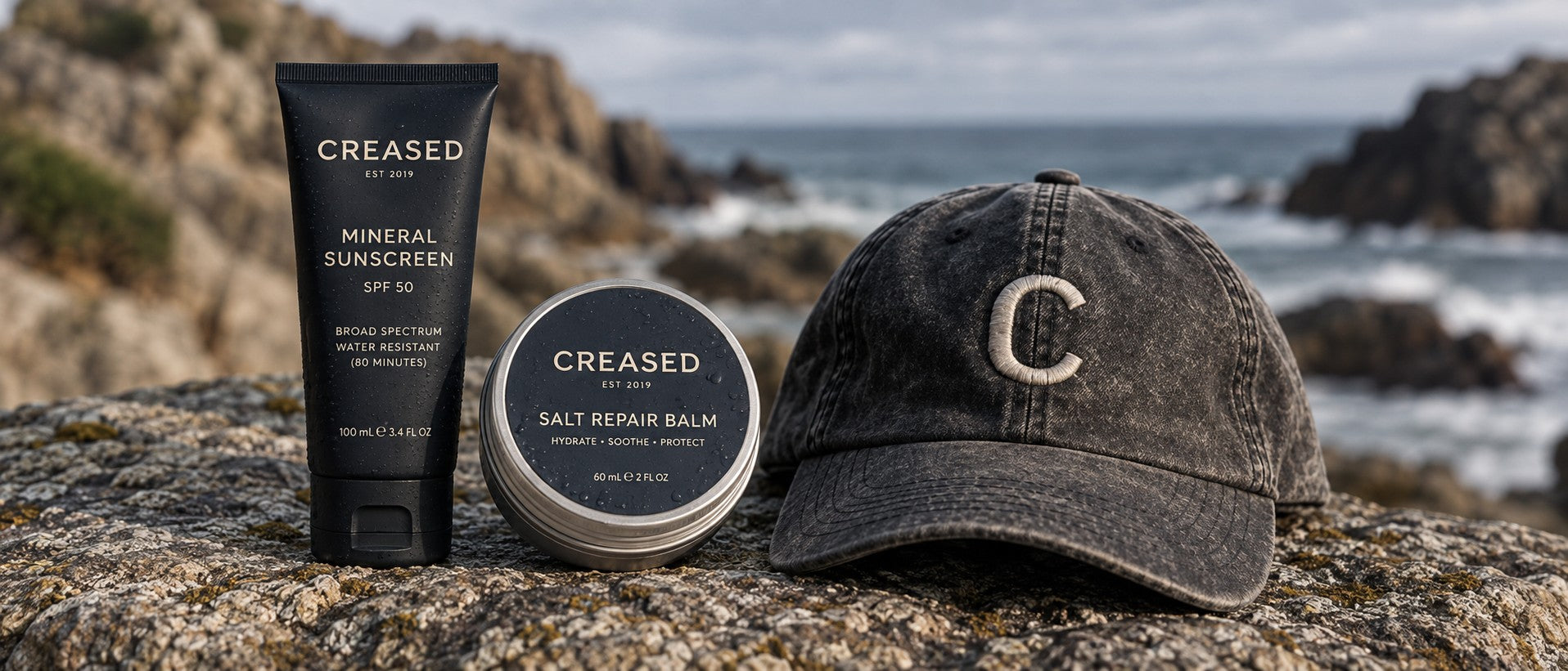 Creased Mineral Sunscreen, Salt Repair Balm and Creased cap on coastal rock