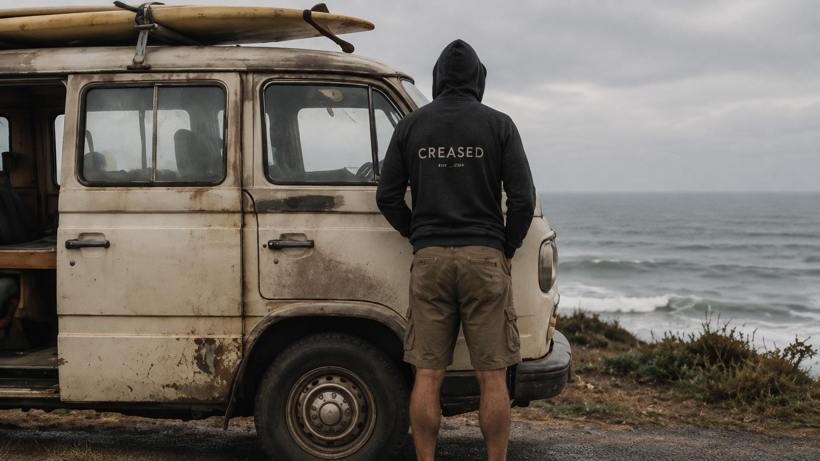 Person in a Creased hoodie beside an old Land Rover with a surfboard on the roof